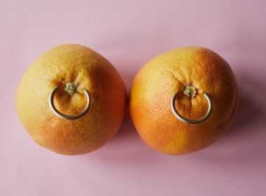 Fresh mandarins with earrings placed on pink surface